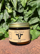 Rowe Naturals sells grass-fed whipped tallow vanilla balm in a glass jar with lush green foliage behind it.
