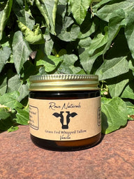 Rowe Naturals sells grass-fed whipped tallow vanilla balm in a glass jar with lush green foliage behind it.
