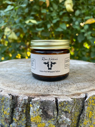 Rowe Naturals grass-fed whipped tallow sits on a textured tree stump against a blurred green background.

