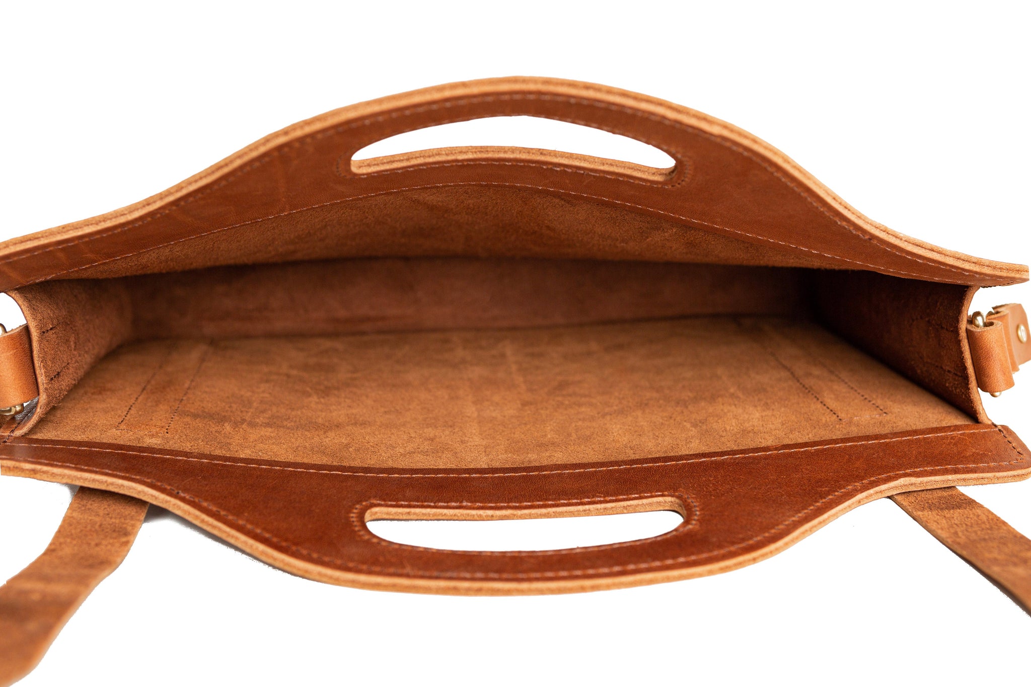 A brown leather tote bag sits open, revealing its spacious, unlined interior.

