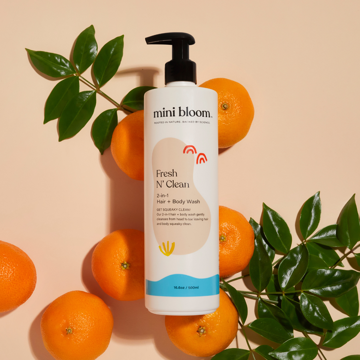 Mini Bloom's Fresh N' Clean 2-in-1 hair and body wash sits among oranges and foliage, highlighting its natural ingredients.
