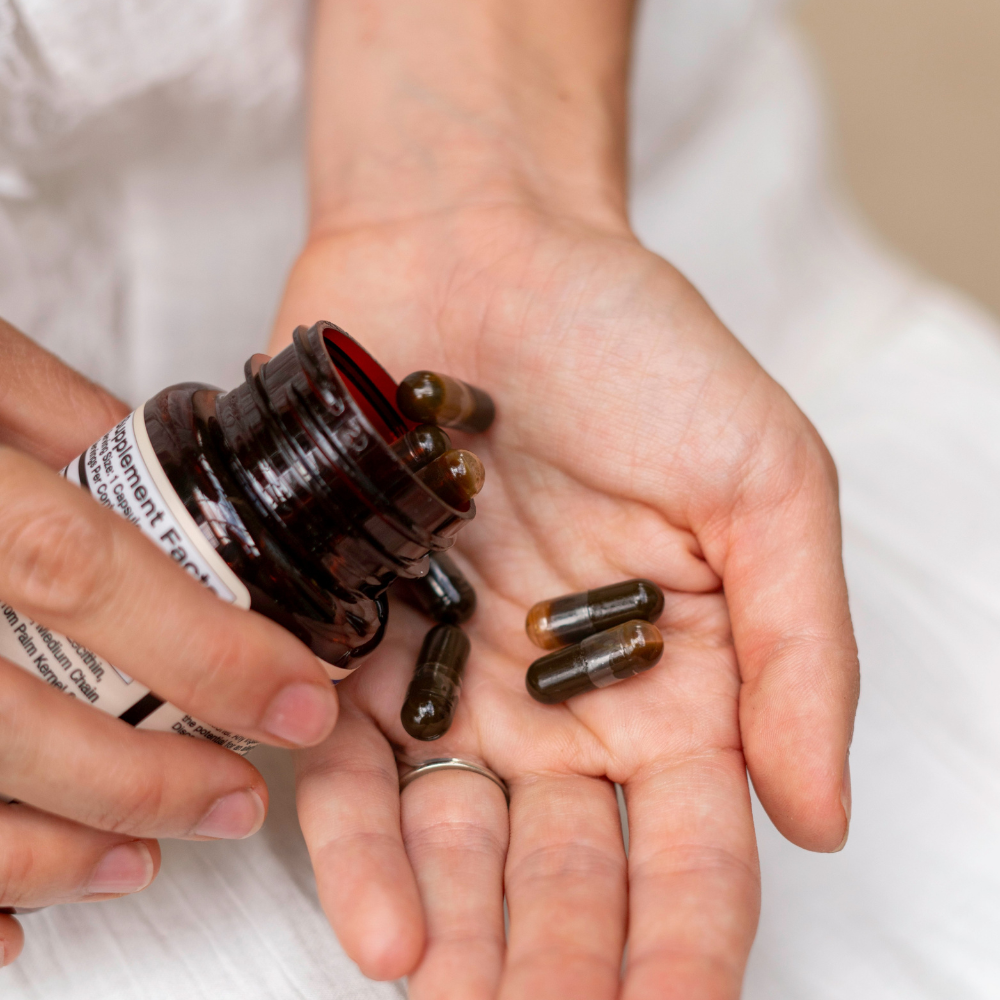 Person pours brown supplement capsules from a bottle into their hand.
