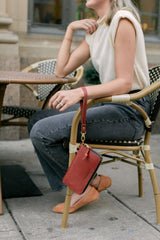 A woman sits at an outdoor cafe with an Urban Originals leather wallet hanging from her chair.
