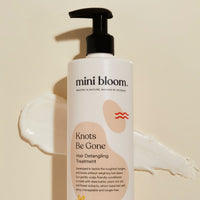 Mini Bloom's "Knots Be Gone" hair detangling treatment bottle sits with a dollop and smear of its conditioner.
