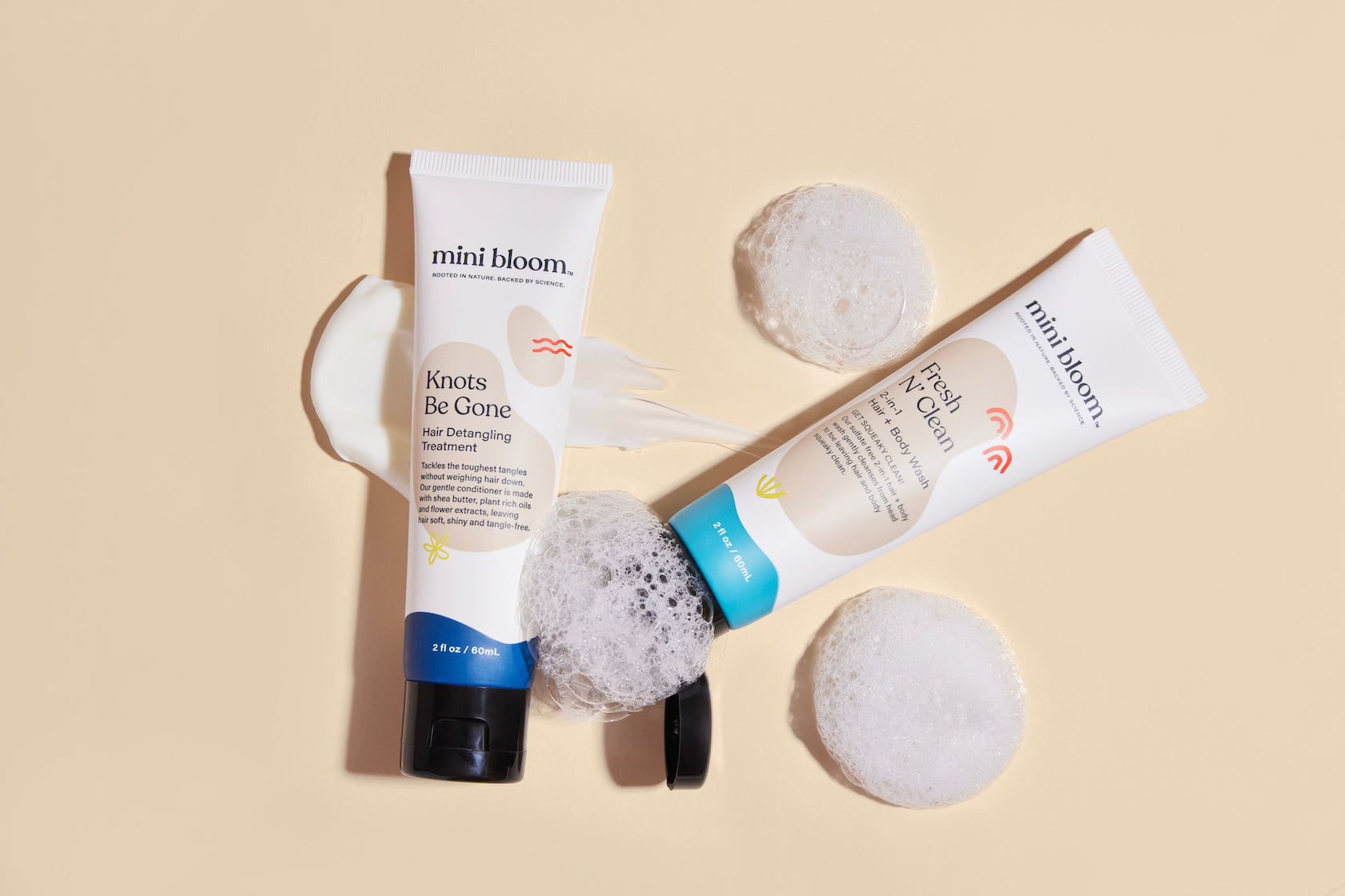Mini Bloom hair detangler and 2-in-1 hair and body wash create suds on a cream background for baby's bath.
