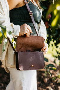 Woman opens her brown leather crossbody bag from Urban Southern outdoors.