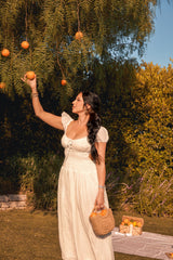 A woman in a white dress picks fresh oranges from a tree during a summer picnic in a sun-drenched orchard.