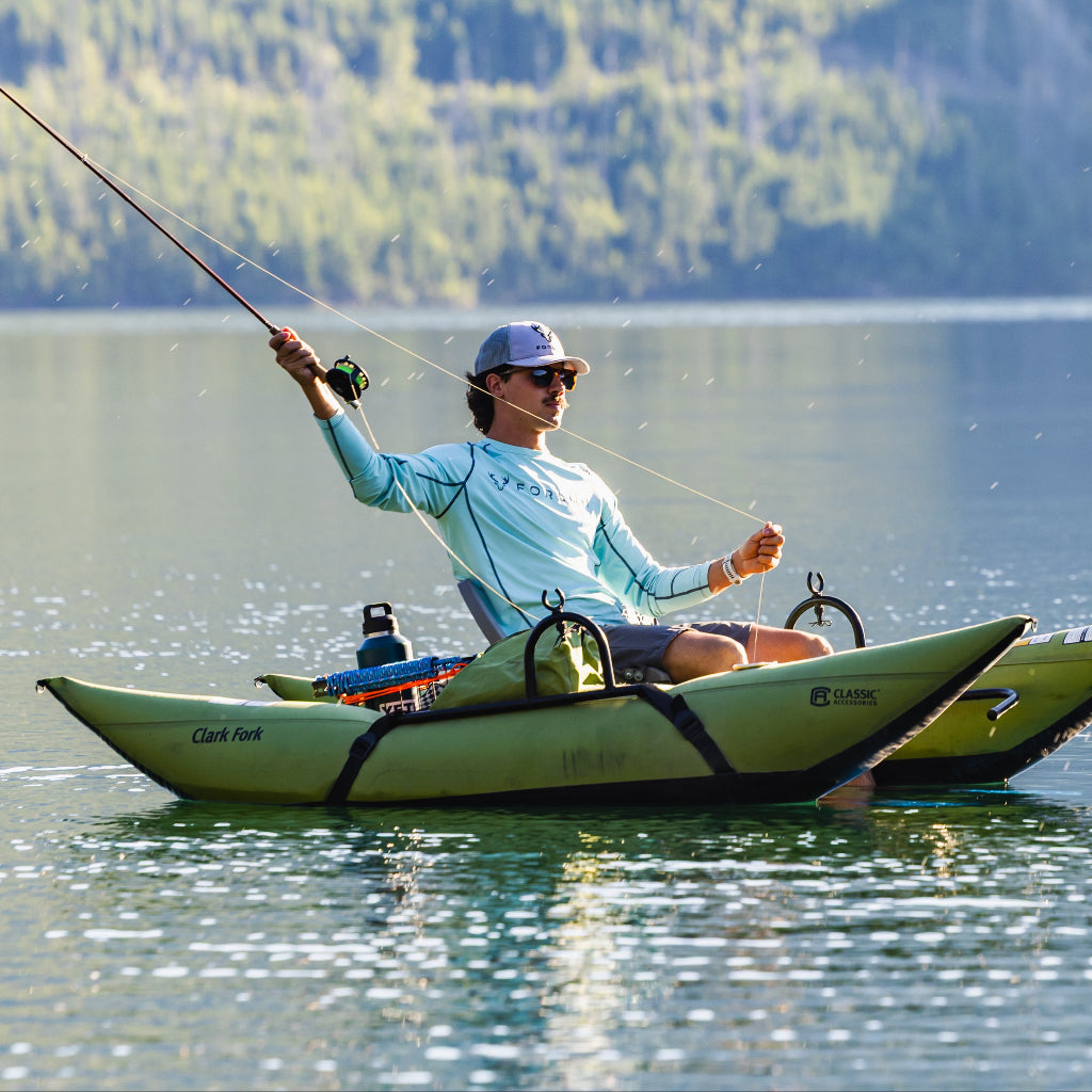 Person fishing from a kayak on a calm lake with mountains in the background