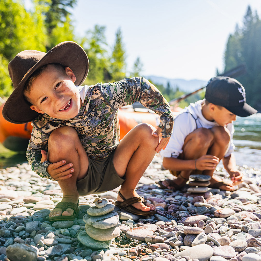 Two children playing by a river with trees in the background