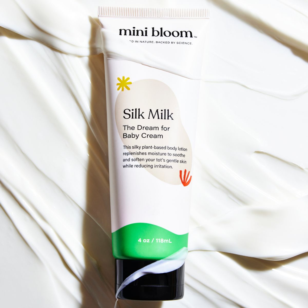 Mini Bloom Silk Milk Baby Cream sits on a background of creamy white lotion.

