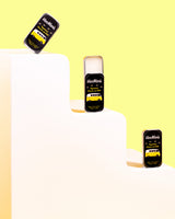 Three tins of VanMan's Peppermint Beeswax Lip Balm, each featuring a yellow VW bus, sit on a stepped white platform against a yellow background.
