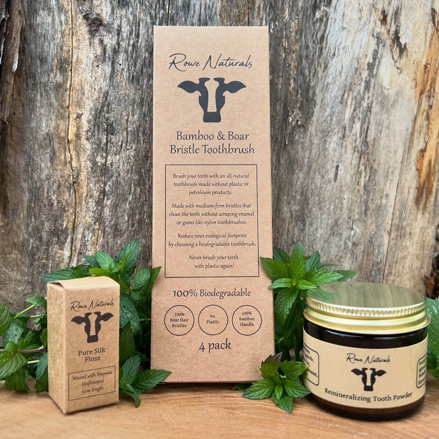 Showcasing Rowe Naturals' plastic-free dental products, including bamboo toothbrushes, silk floss, and remineralizing tooth powder, arranged with fresh mint sprigs against a wood backdrop.

