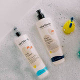 Mini Bloom baby bath products, including hair and body wash and detangling treatment, sit in a bubbly bathtub.
