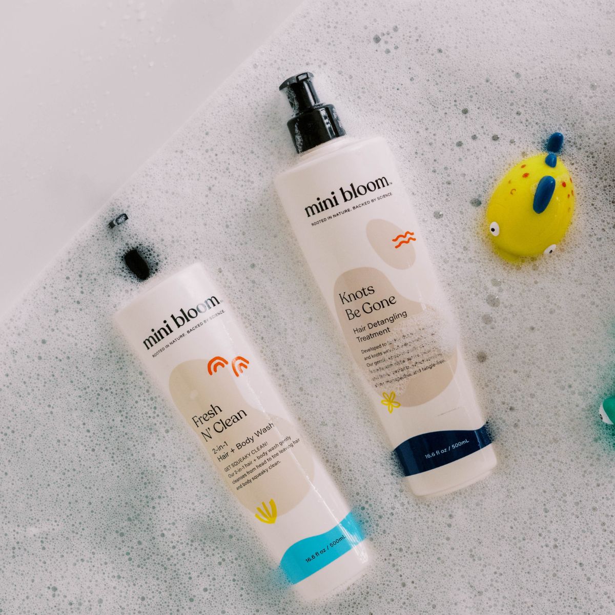 Mini Bloom baby bath products, including hair and body wash and detangling treatment, sit in a bubbly bathtub.
