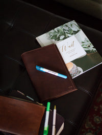 A journal, devotional titled "Wait: A Walk Through The Psalms," and a pen labeled "pray" rest on a dark leather ottoman, suggesting quiet time for reflection.
