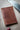 A handcrafted leather journal sits on a workbench next to a saw, suggesting a workshop environment.
