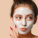 Woman applies a facial beauty mask with red manicured nails.
