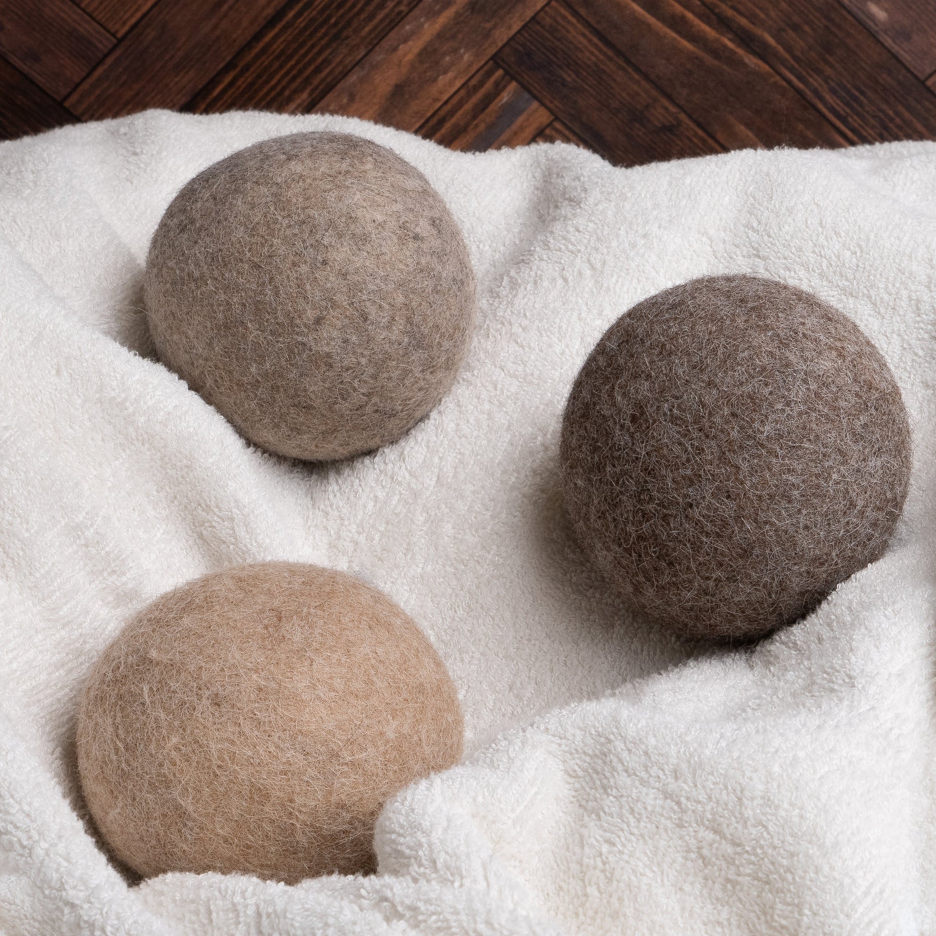 Three wool dryer balls rest on a soft, white terry towel against a dark wooden background.
