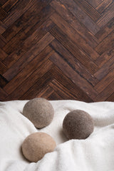 Three woolen dryer balls sit atop a fluffy white towel against a rustic herringbone wood background.
