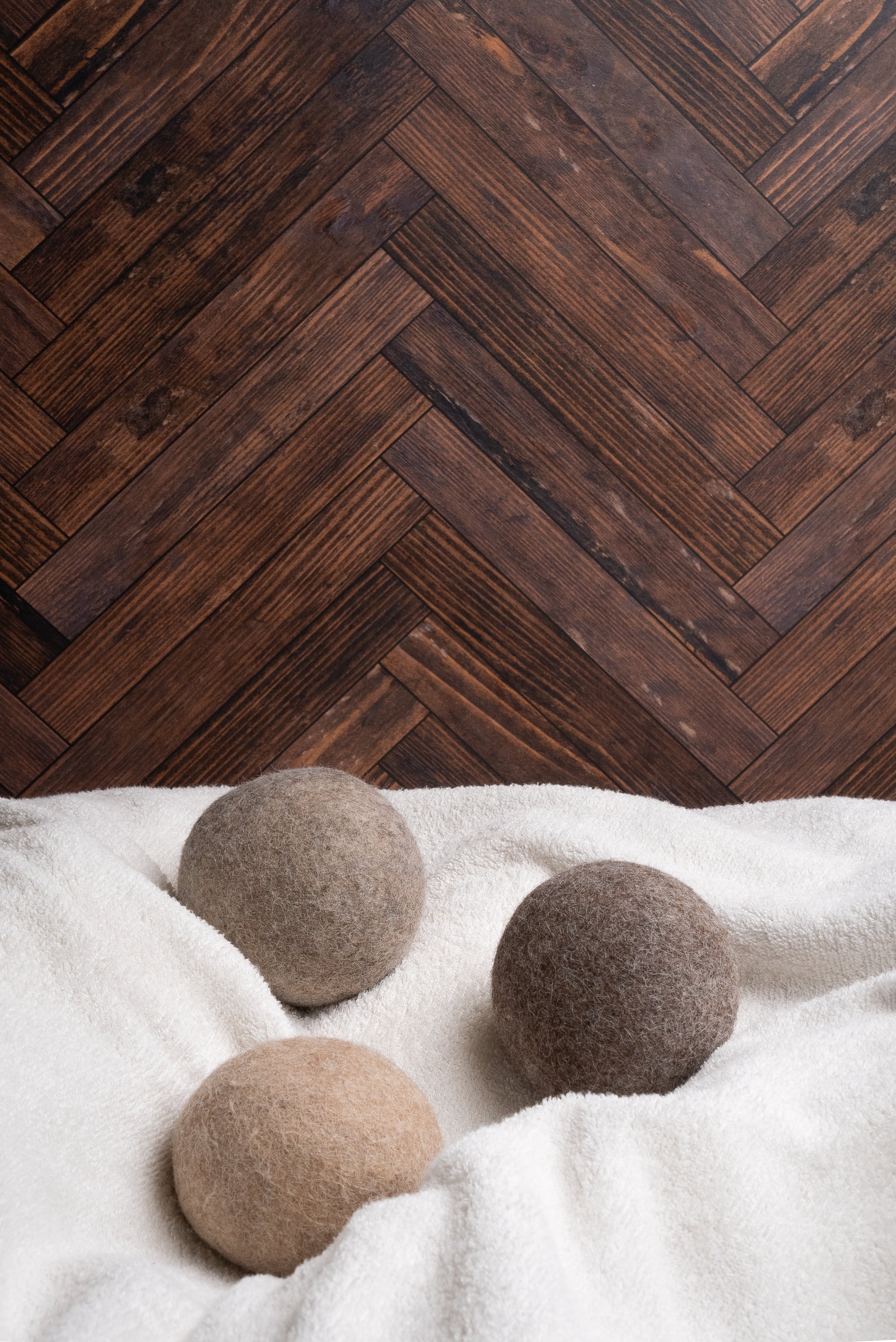 Three woolen dryer balls sit atop a fluffy white towel against a rustic herringbone wood background.
