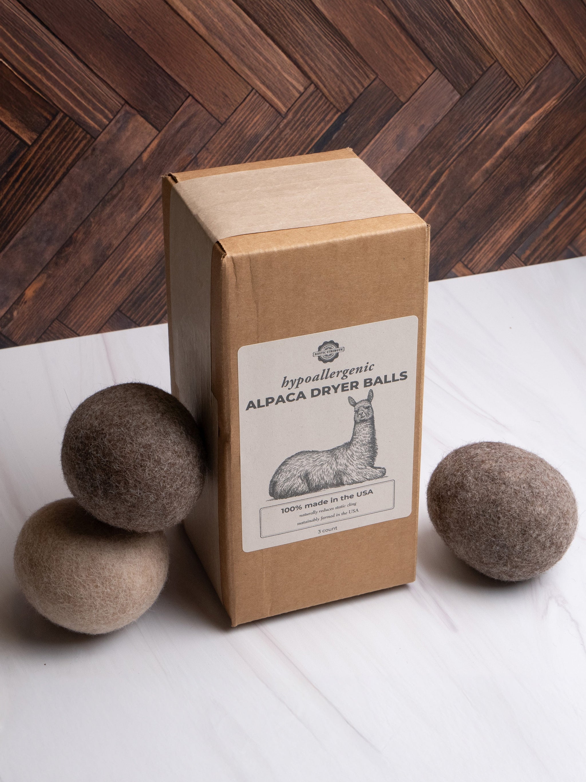 A package of hypoallergenic alpaca wool dryer balls sits near loose dryer balls on a marble surface.
