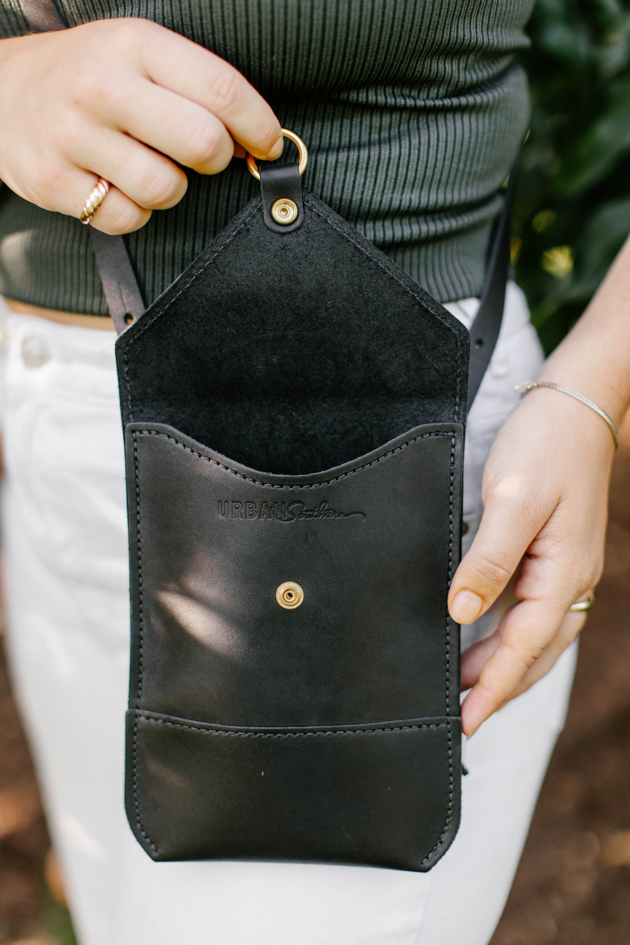 Person showcases an open black leather Urban Southern crossbody phone bag.
