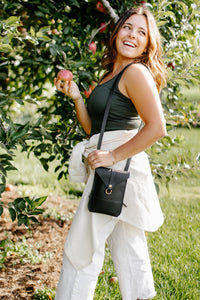 A smiling woman holds a freshly picked apple while standing in an apple orchard during a sunny day.
