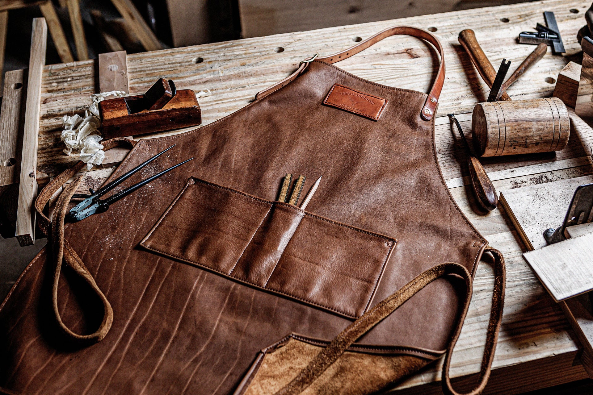 A leather woodworking apron lies on a workbench surrounded by carpentry tools.
