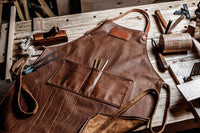 A leather woodworking apron lies on a workbench surrounded by carpentry tools.
