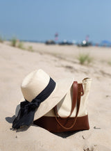 Beach bag and sun hat sit on the sand, inviting relaxation and vacation vibes.
