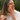 Woman applying cream to her face outdoors, holding a jar of the same cream.