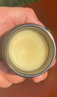 A hand holds an open container of smooth, yellow, natural skincare balm.
