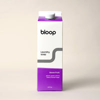 Bloop brand laundry soap, in stone fruit apricot peach plum scent, sits on a cream-colored surface.

