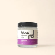 Bloop laundry soap sits in a clear jar, advertising a stone fruit scent of apricot, peach, and plum.
