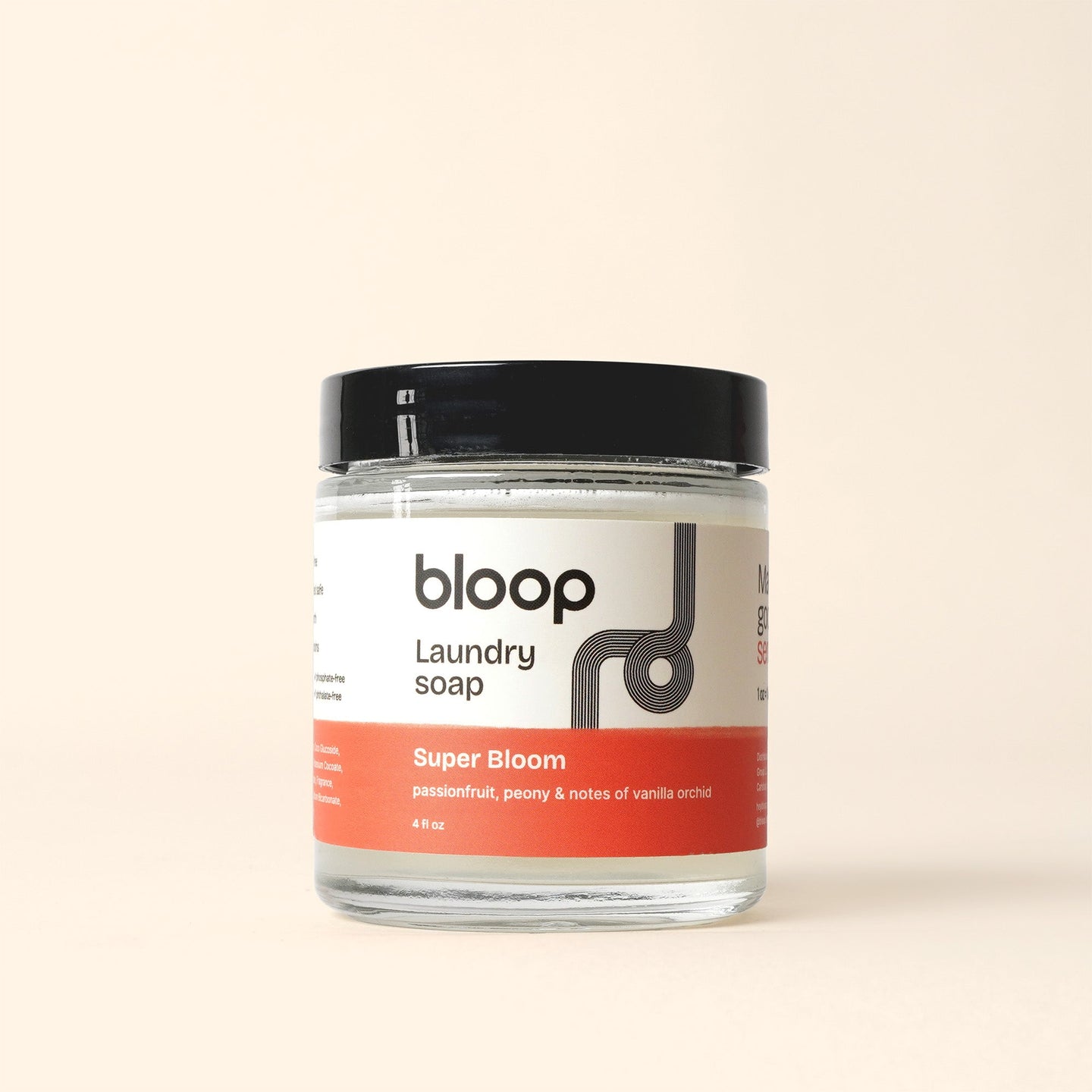 Showcasing Bloop's Super Bloom laundry soap, a fragrant blend of passionfruit, peony, and vanilla orchid, in a clear glass jar with a black lid.
