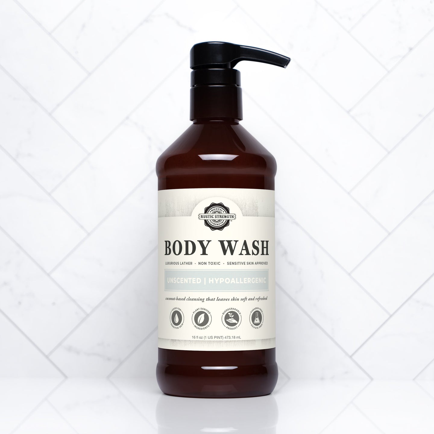 A brown bottle of Rustic Strength body wash, labeled unscented and hypoallergenic, sits against a white marble tile background.

