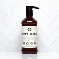 A brown bottle of Rustic Strength body wash, labeled unscented and hypoallergenic, sits against a white marble tile background.
