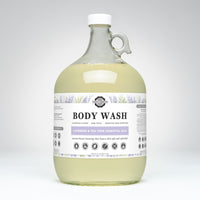 View a one-gallon glass jug of Rustic Strength body wash featuring lavender and tea tree essential oils, promising luxurious lather and gentle cleansing for sensitive skin.
