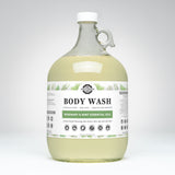 A one-gallon jug displays Rustic Strength rosemary mint essential oil body wash, emphasizing its natural, sensitive skin-friendly formula.
