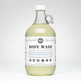 Rustic Strength's unscented body wash, a coconut-based cleanser in a clear glass jug, promises luxurious lather and is suitable for sensitive skin.
