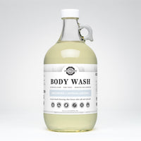 Rustic Strength's unscented body wash, a coconut-based cleanser in a clear glass jug, promises luxurious lather and is suitable for sensitive skin.
