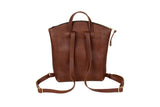 A brown leather backpack displays its adjustable straps, top handle, and zipped closure against a white background.
