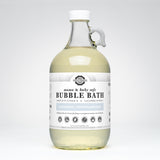 A clear glass jug displays Rustic Strength mama & baby safe unscented bubble bath, highlighting its vitamin B and cucumber extract ingredients.
