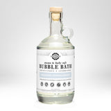 Rustic Strength presents its mama and baby safe, unscented, hypoallergenic bubble bath in a clear glass bottle with a cork stopper.
