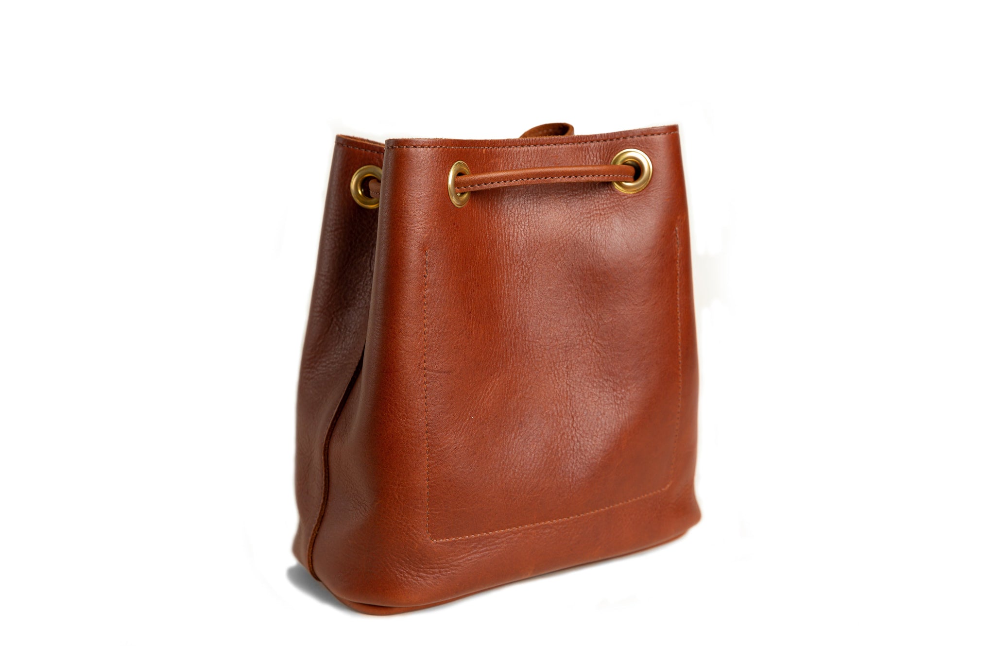 A brown leather bucket bag with gold grommets sits on a white background.