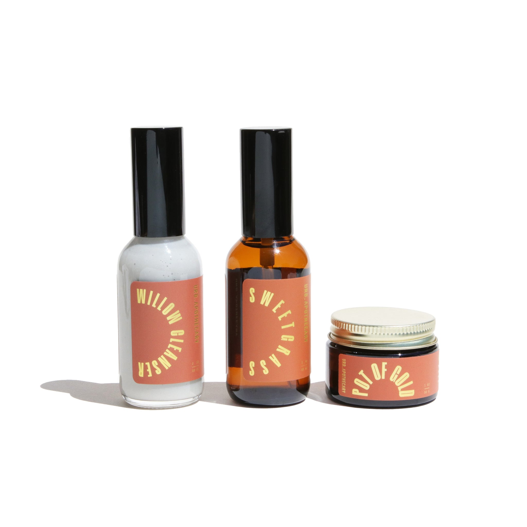 Three URB Apothecary skincare products, including Willow Cleanser, Sweetgrass spray, and Pot of Gold cream, sit on a white surface.
