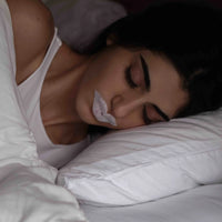 A woman sleeps peacefully with a mouth tape strip on, promoting nasal breathing and better sleep quality.
