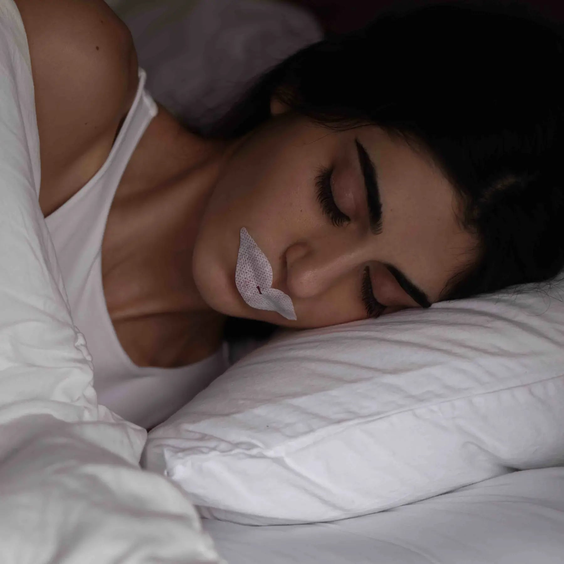 A woman sleeps peacefully with a mouth tape strip on, promoting nasal breathing and better sleep quality.
