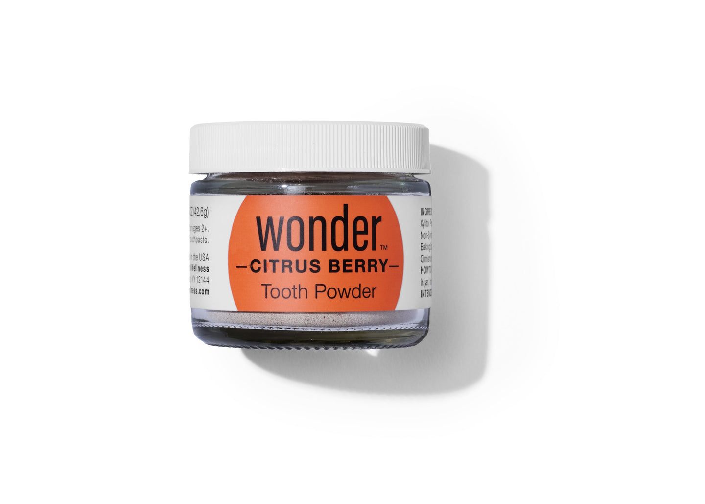 A glass jar with a white lid holds Wonder Citrus Berry tooth powder on a white background.
