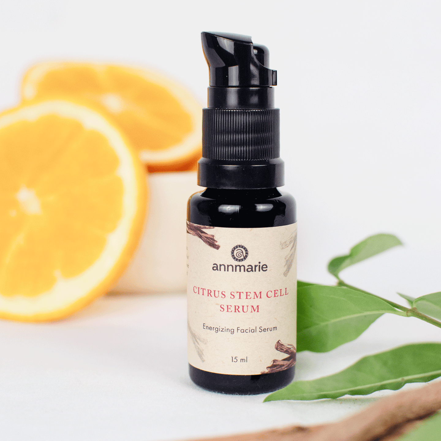 Annmarie Citrus Stem Cell Serum bottle sits next to fresh orange slices and green leaves.

